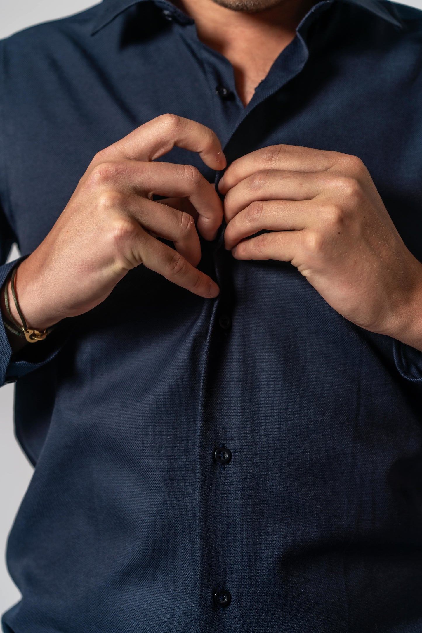 Detail van man die donker blauw effen hemd van Suitify dichtknoopt